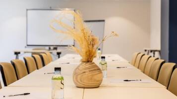 A conference room with a long table, chairs, a projector screen, and a vase with dried plants.