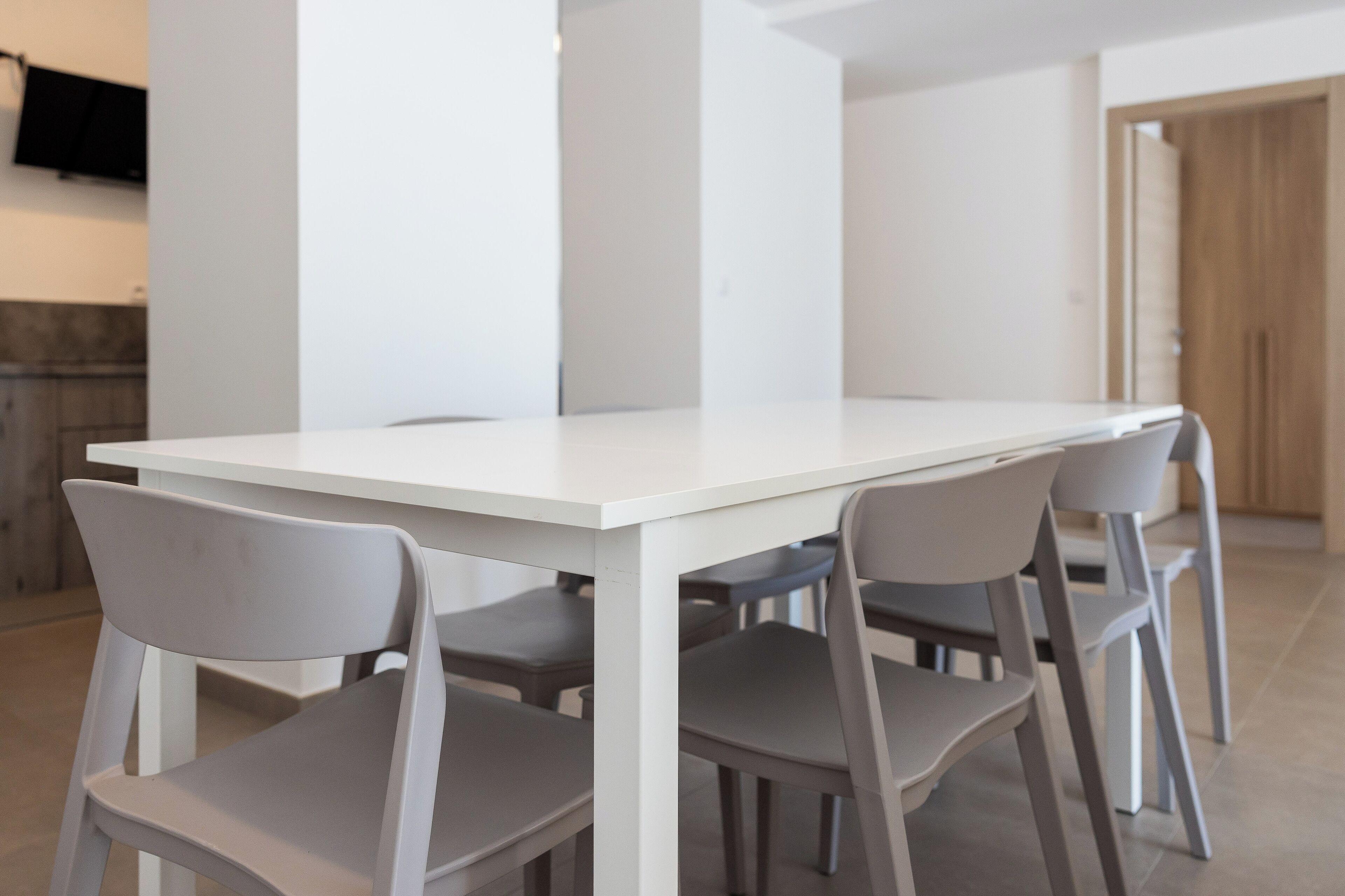 A modern dining area with a white table and four grey chairs.