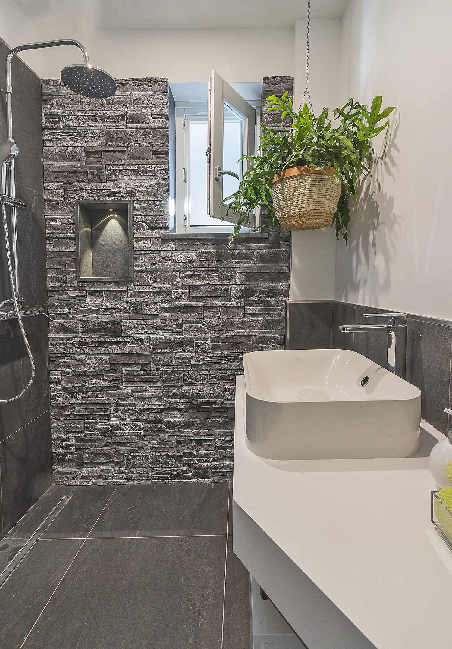 Une salle de bain moderne avec un mur en pierre, un grand lavabo et une plante suspendue.