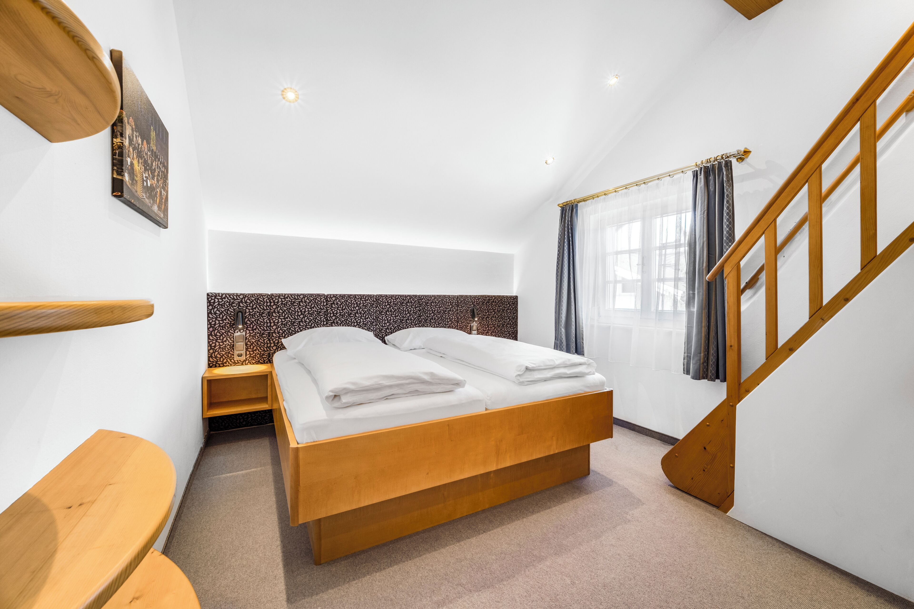 Ein Schlafzimmer mit einem hölzernen Bett, einem Nachttisch, einer Holzbank, einem Stadtbildgemälde und einer Treppe.