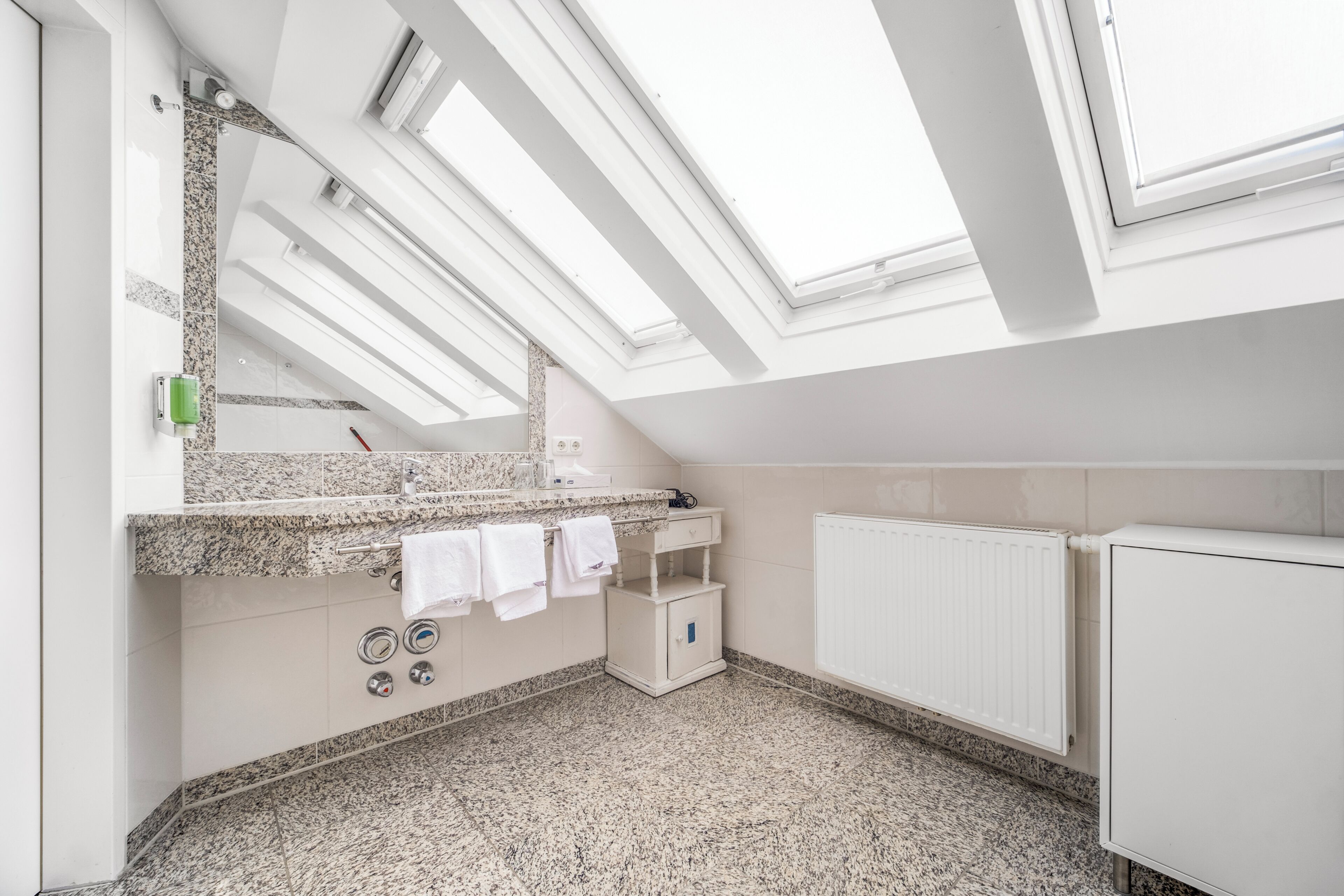 Ein modernes Badezimmer mit Dachfenstern, einer Granitmarmortheke, einem weißen Heizkörper und einem kleinen Schrank.