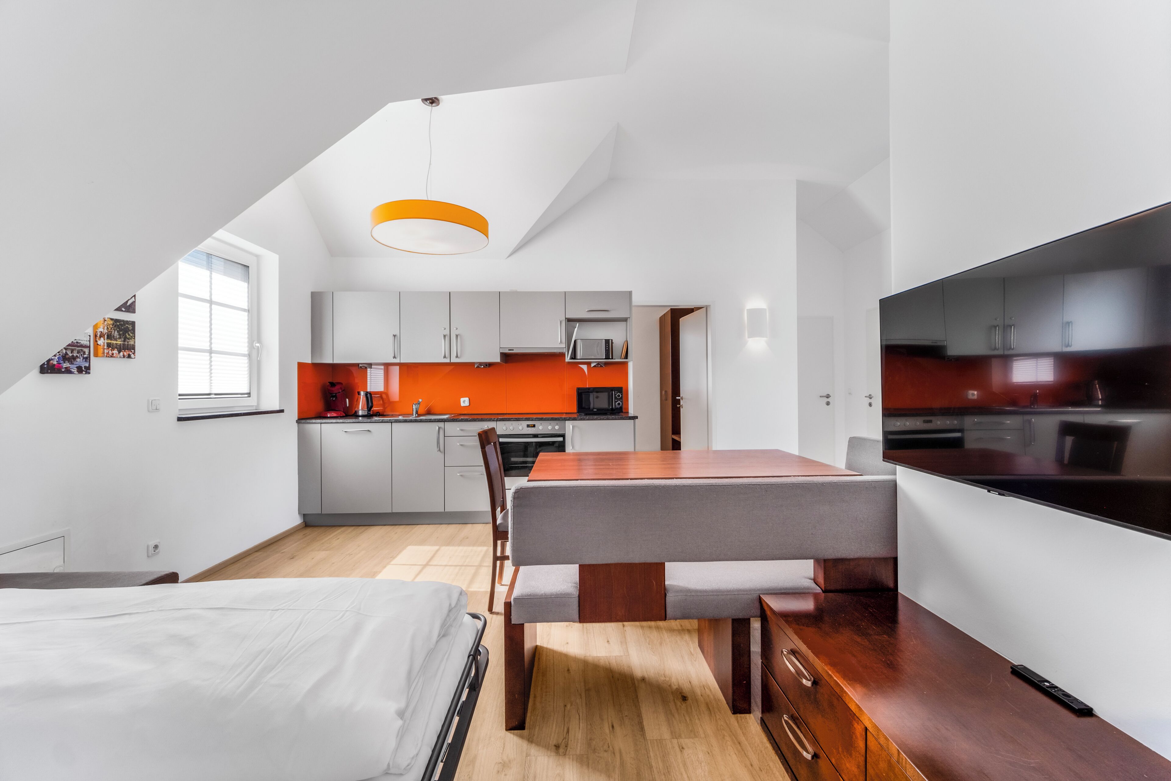 A modern kitchen with white cabinets, a wooden dining table, and a large TV.