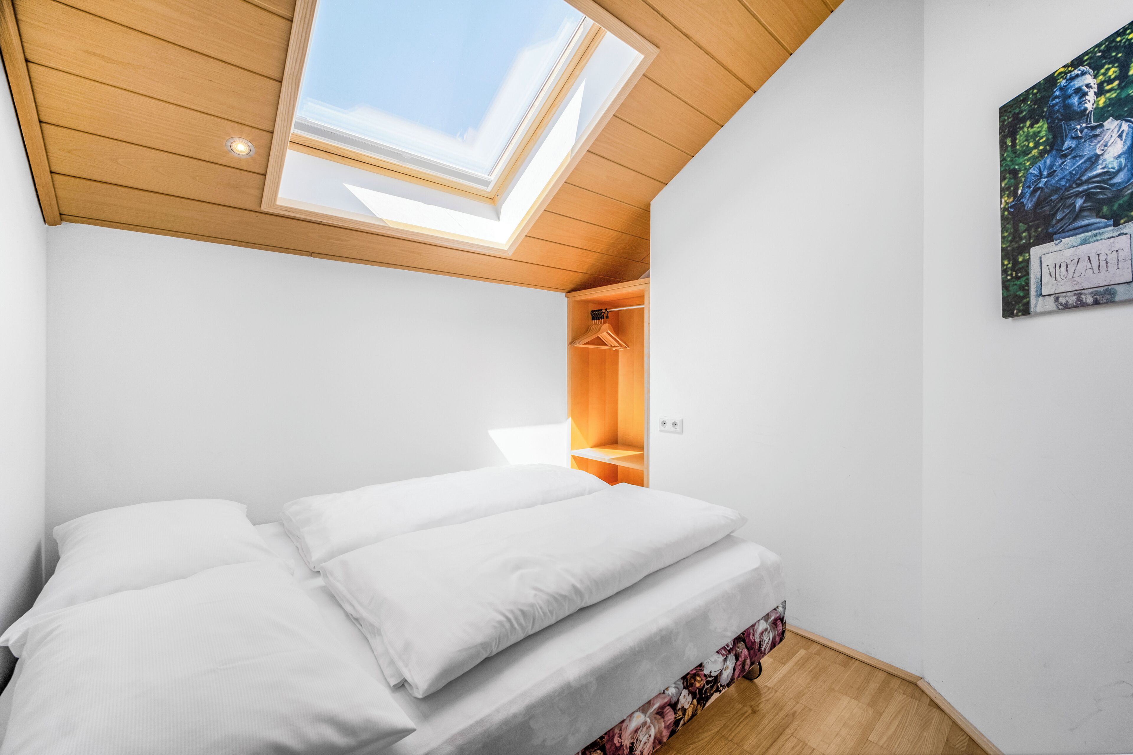Ein Schlafzimmer mit Dachfenster, einem Bett mit weißen Bettwäsche, einem Holzschrank und einem an der Wand befestigten Gemälde.