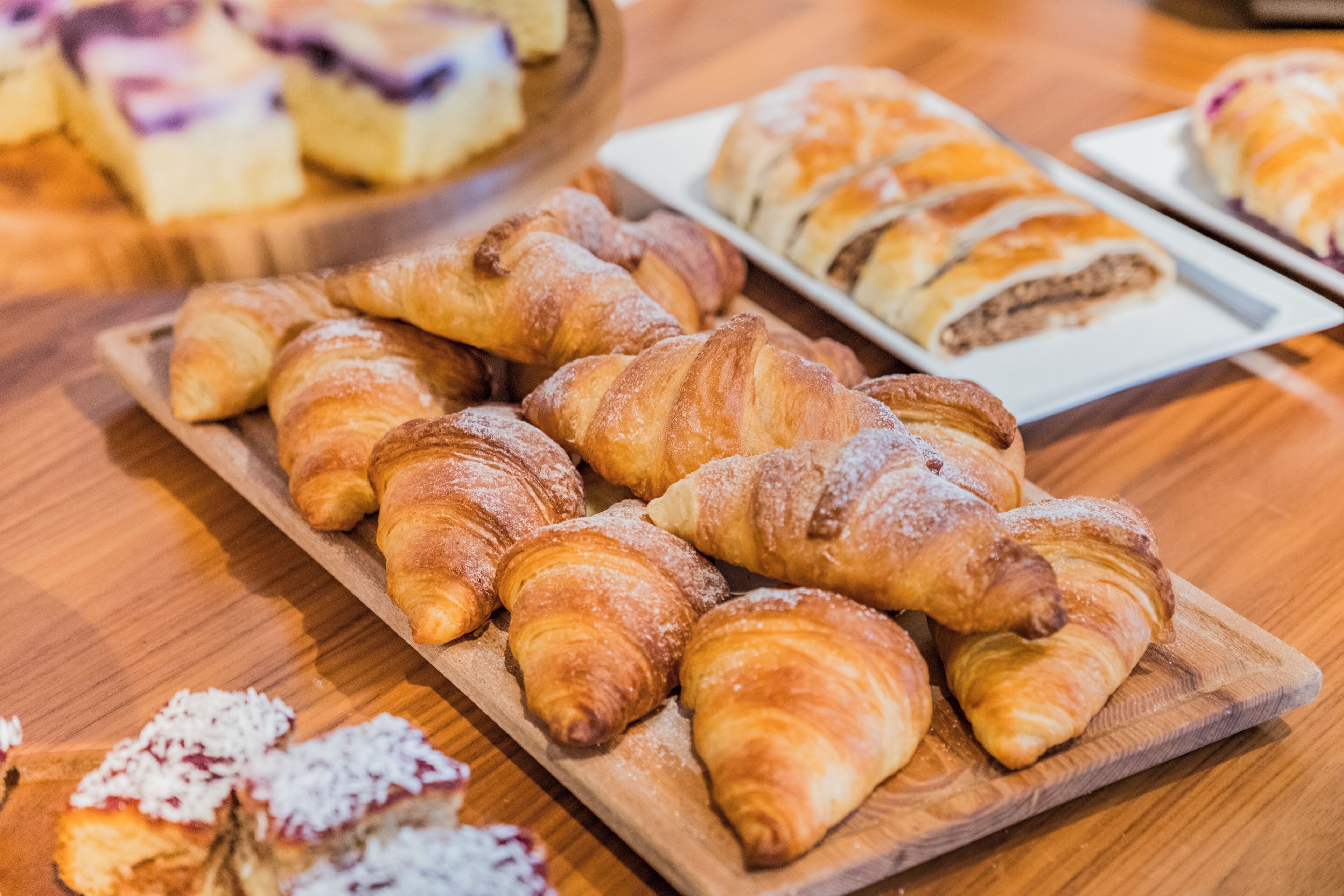 A wooden board with assorted pastries, including croissants and a dessert with fruit.