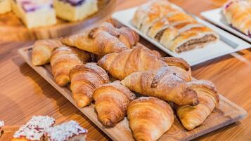 A wooden board with assorted pastries, including croissants and a dessert with fruit.