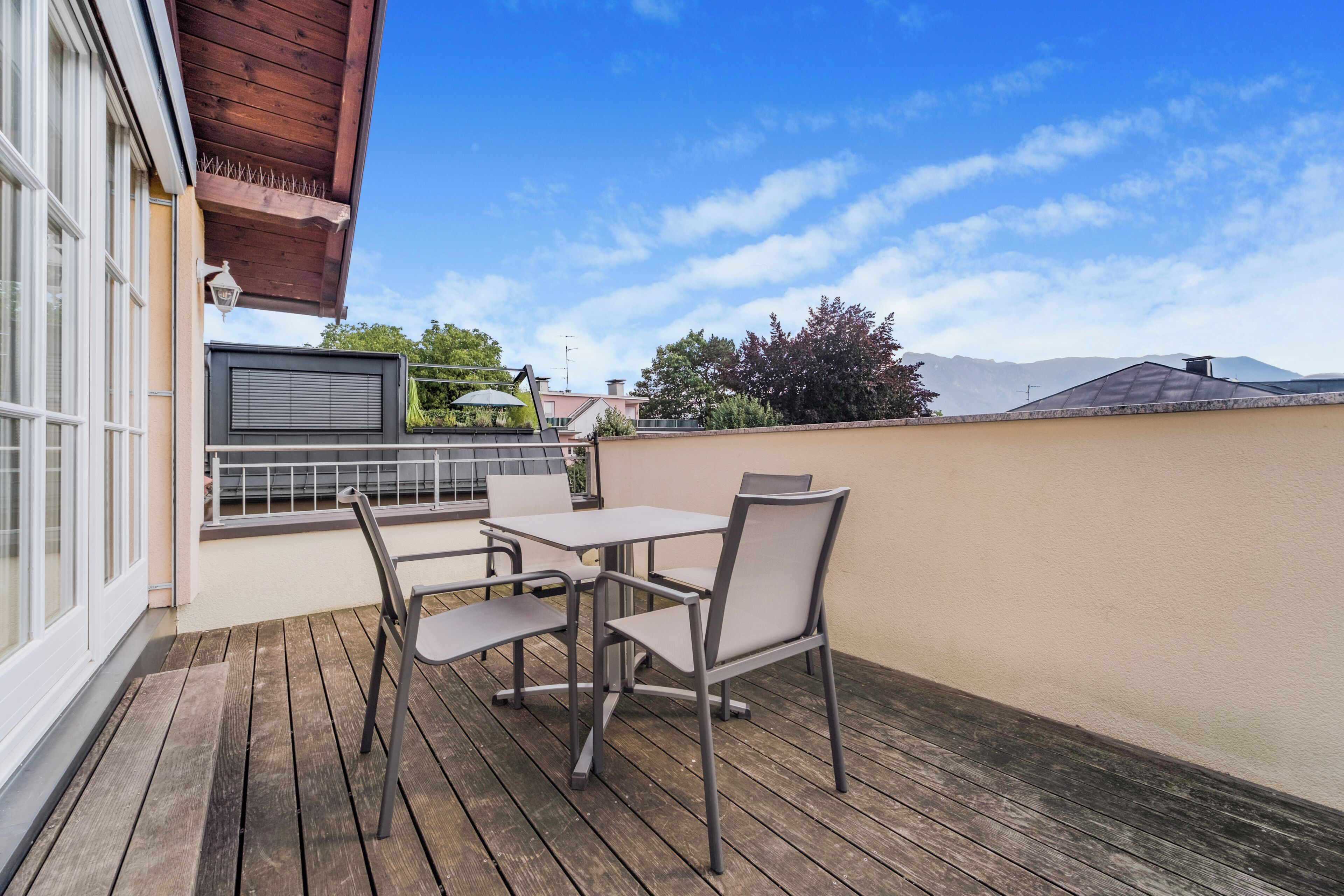 An outdoor deck with a table and chairs, a pergola, and a view of the surrounding area.