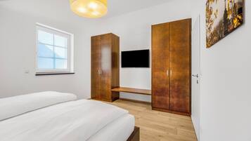 A bedroom with a bed, a TV, wooden wardrobes, a bench, and a window.