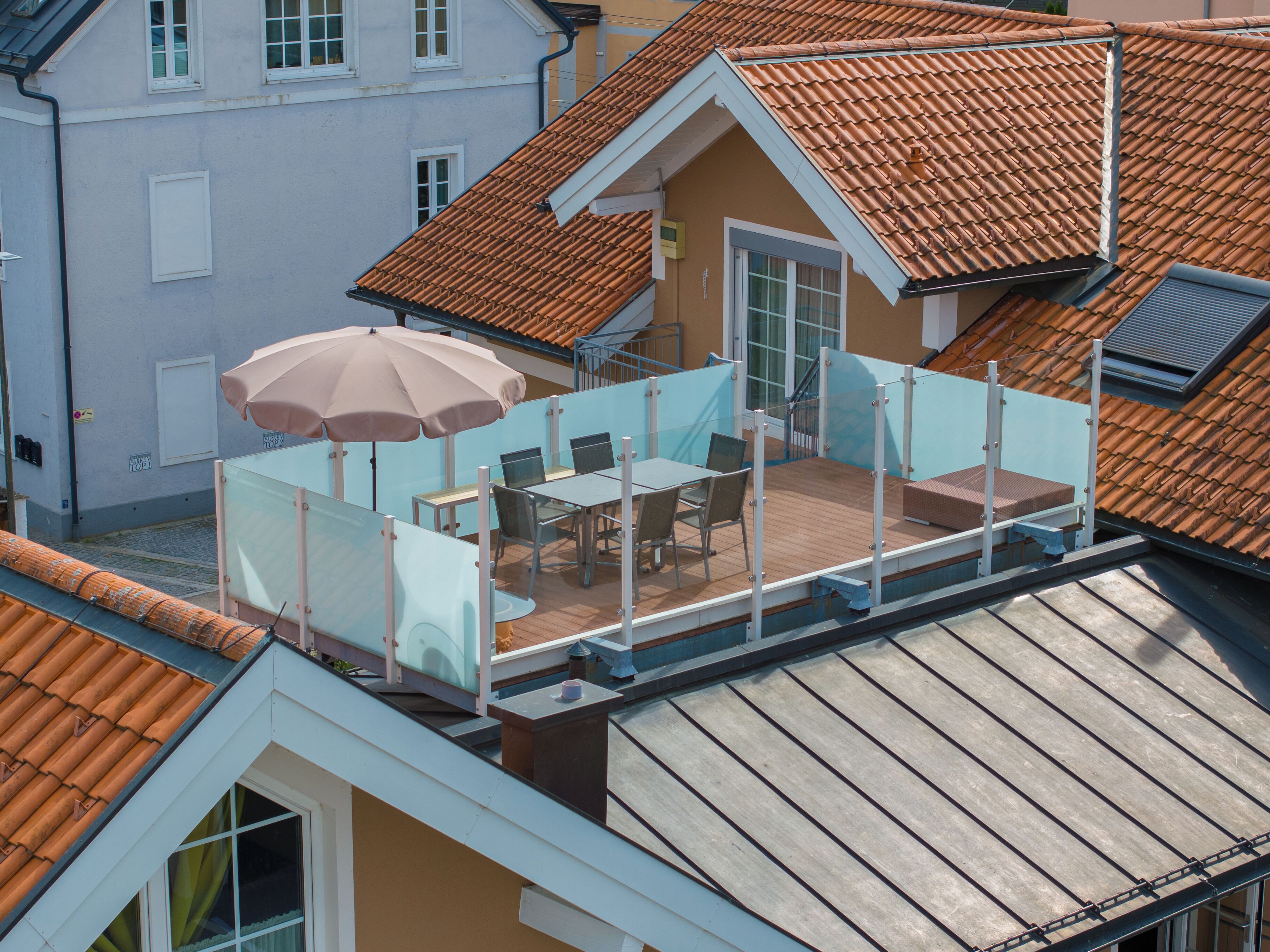 A rooftop terrace with a table and chairs, a large umbrella, and a glass railing.