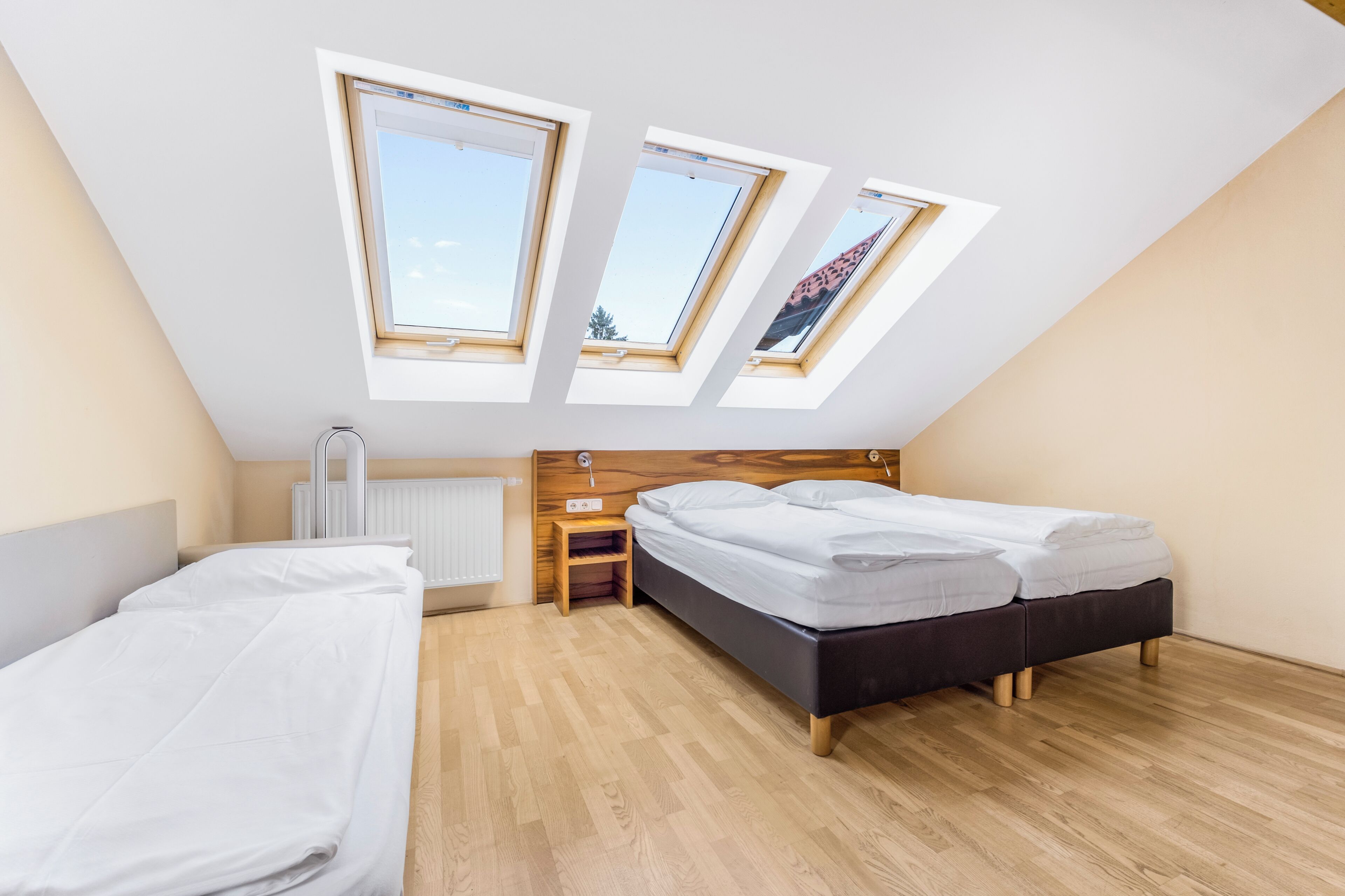 Ein Schlafzimmer mit schrägen Wänden, zwei Betten, einem Nachttisch, einem Heizkörper und Dachfenstern.