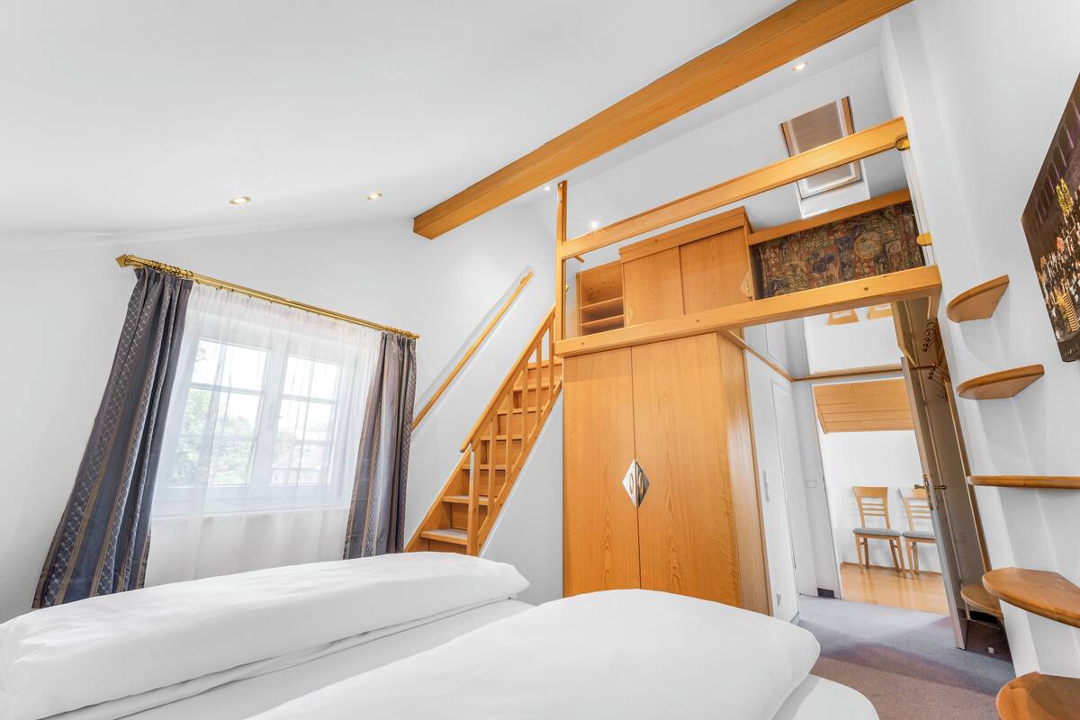 Un dormitorio con cama, una escalera de madera, un armario y vistas a un comedor.