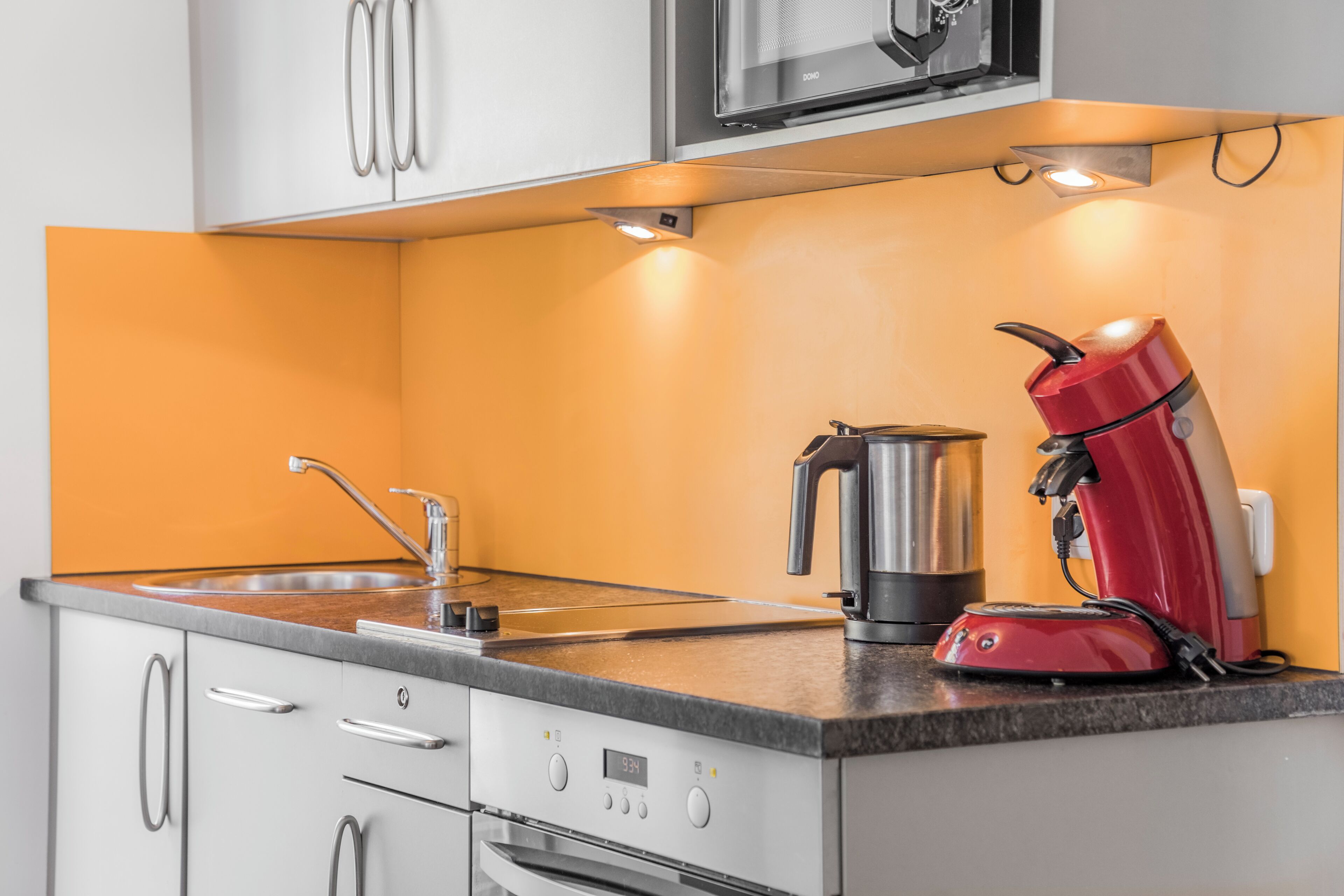 Une cuisine équipée d’un four à micro-ondes, d’une machine à café et d’une bouilloire, le tout posé sur le plan de travail.