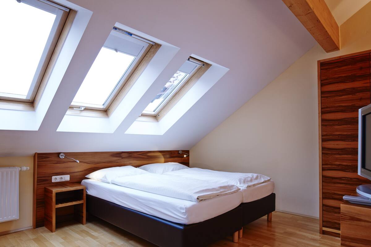 Un dormitorio con techo inclinado, tragaluces, una cama, una mesita de noche y un mueble para televisor.