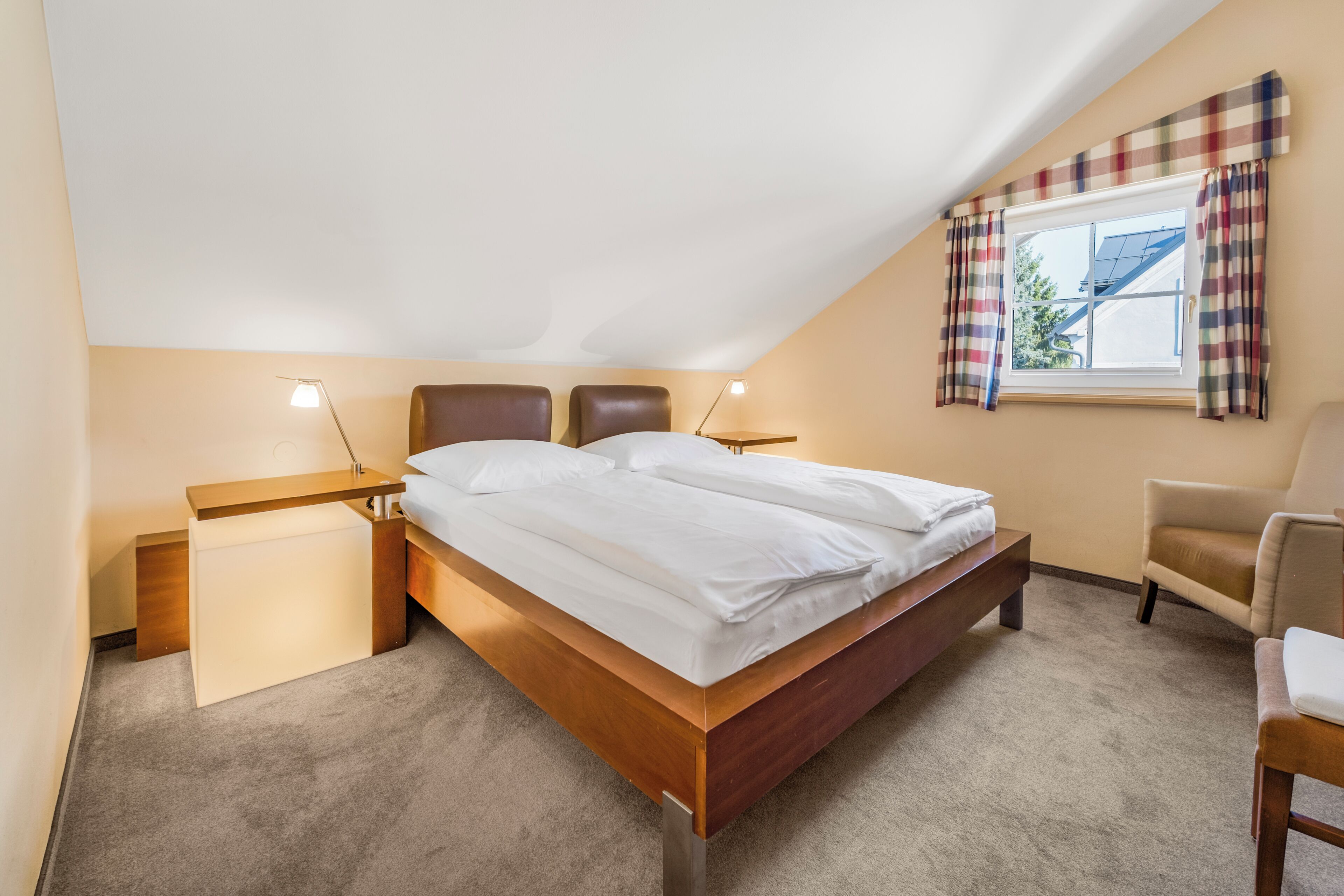 Ein Schlafzimmer mit einem Bett, Nachttischen, einem Sessel und einem Fenster mit Vorhängen.