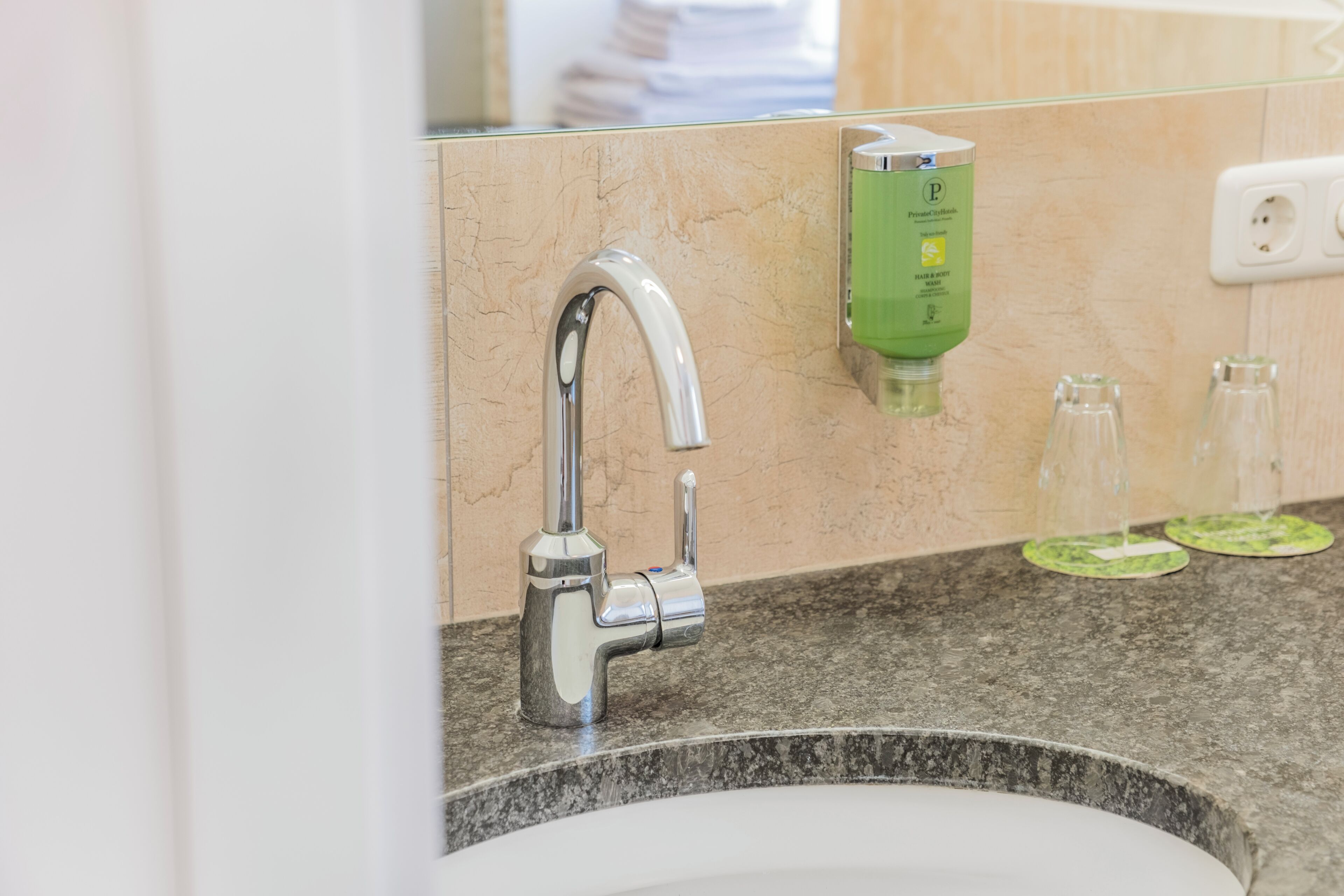 A bathroom sink with a modern faucet, a soap dispenser, and a mirror reflecting a person.