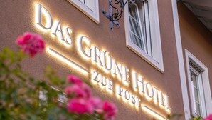 En hotellskylt med namnet ”Das Grüne Hotel Zur Post” som är upplyst.