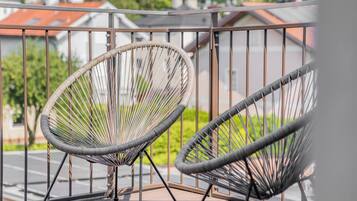 Two wicker chairs on a balcony with a metal railing, overlooking a residential area.