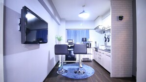 A compact kitchen with a TV mounted on the wall, a dining area with two chairs, and a blue rug. - MG103 Cozy and clean room SHINAGAWA (品川区)