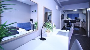 A modern living room with a blue sofa, a desk with a laptop, a large mirror, and a potted plant. - MG103 Cozy and clean room SHINAGAWA (品川区)