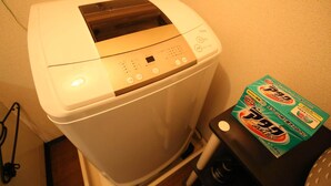 A compact, white portable washing machine with a digital control panel, placed next to a black cart with a detergent box. - MG103 Cozy and clean room SHINAGAWA (品川区)