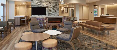 A modern hotel lobby with a fireplace, comfortable seating, a reception desk, and a television.