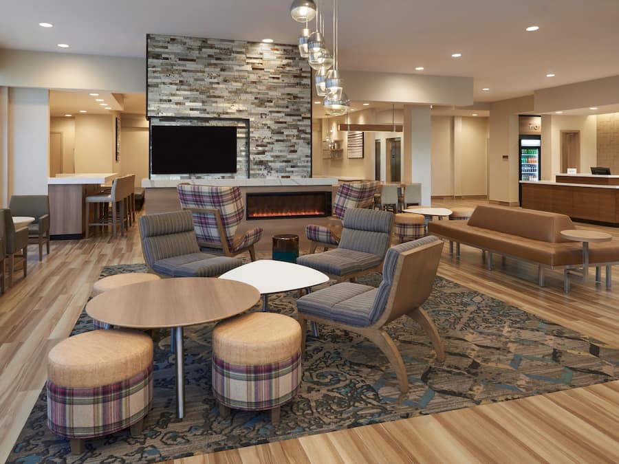 A modern hotel lobby with a fireplace, comfortable seating, a reception desk, and a television.