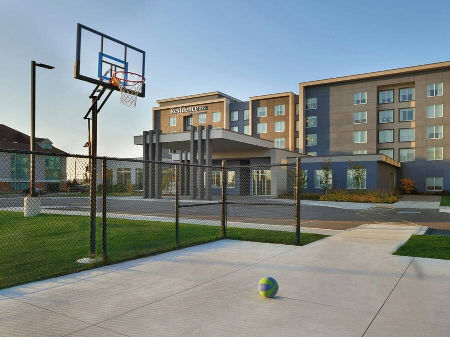 Ein Basketballplatz mit Netz und Ball, einem Zaun und einem Gebäude mit der Aufschrift 'Residence Inn'.