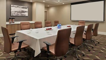 A conference room with a long table, brown chairs, a projector screen, and a whiteboard.