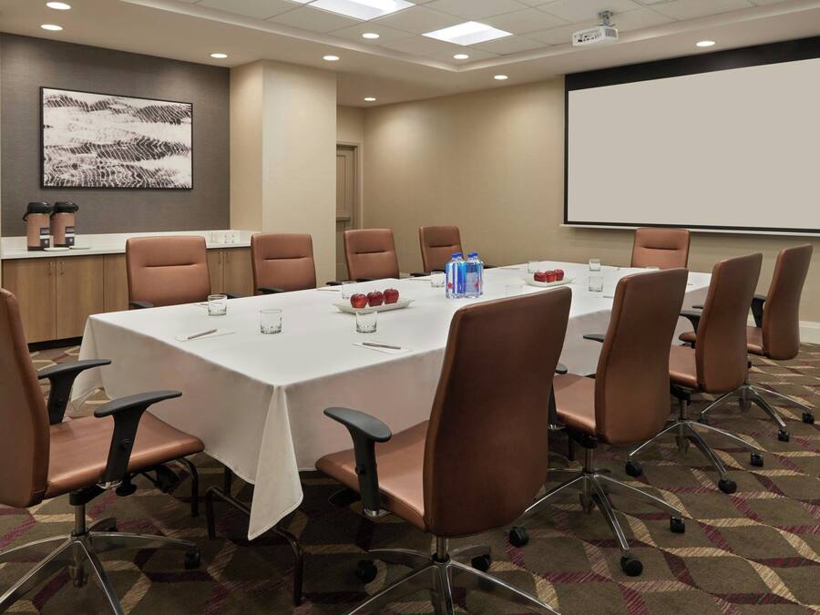 A conference room with a long table, brown chairs, a projector screen, and a whiteboard.