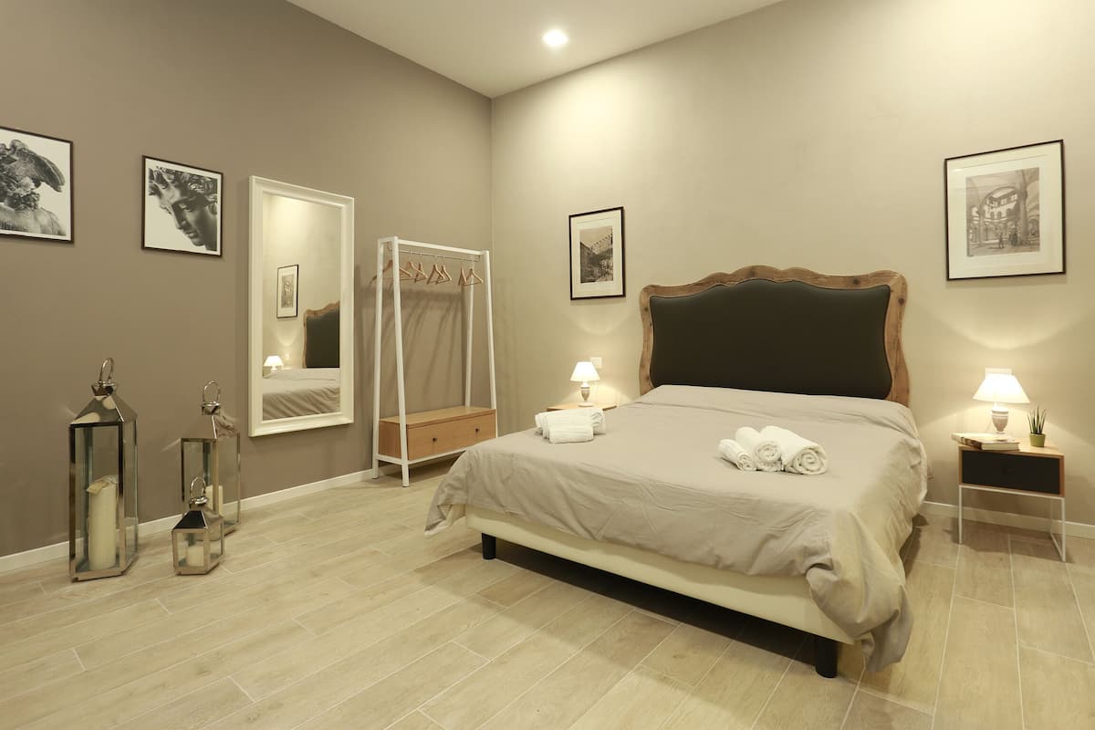 A neatly arranged bedroom with a large bed, bedside lamps, a wardrobe, and framed artwork on the walls.