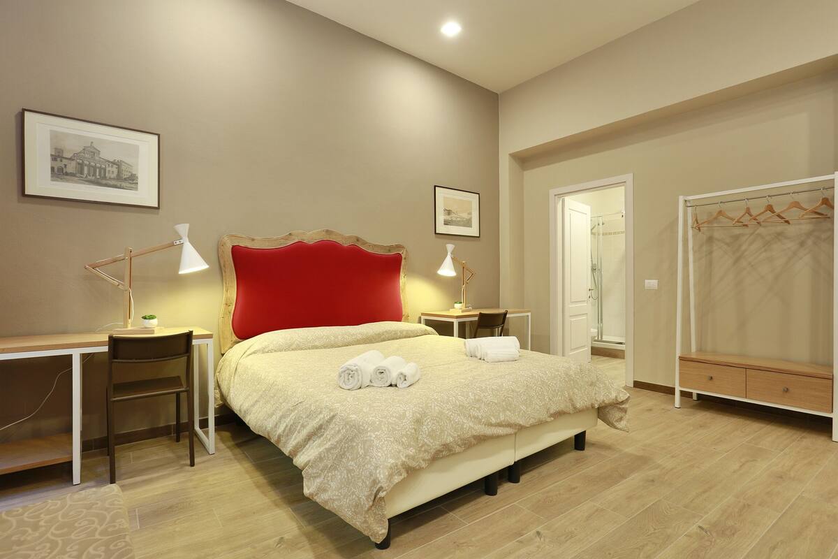 A neatly arranged bedroom with a bed, bedside tables, a desk, and a wardrobe.