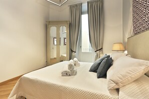 A neatly made bed with rolled towels, a bedside lamp, and a patterned headboard. - Tornabuoni Boutique (Florence)