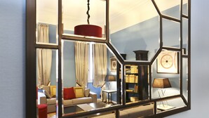 Ein Zimmer mit einem geometrischen Spiegel, der einen Wohnbereich, ein Sofa, einen Couchtisch, eine Lampe und ein Bücherregal reflektiert.