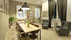 Ein modernes Wohnzimmer mit Essbereich, mit einem großen Holztisch, mehreren Stühlen, einem grauen Sessel und einer Stehlampe.