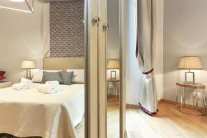 A hotel room with a bed, two bedside lamps, a mirror, a patterned wall, and a wooden floor. - Tornabuoni Boutique (Florence)