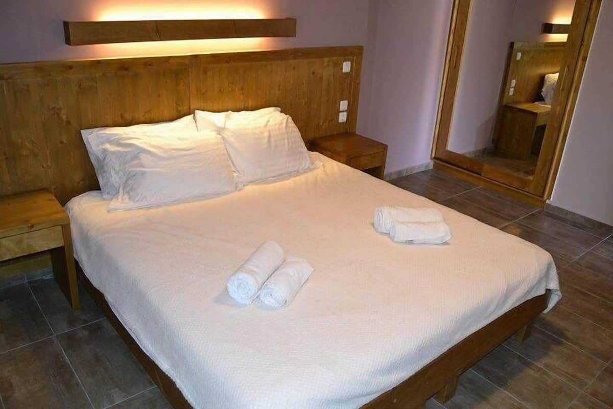 Un lit bien fait, avec du linge de lit blanc et des serviettes pliées, une tête de lit en bois et une table de chevet avec une lampe.