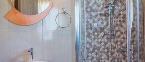 Une salle de bain avec un lavabo blanc, un miroir rond et une douche en verre, le mur étant recouvert de carreaux à motifs.