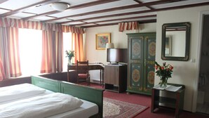 Une chambre d’hôtel comprenant un lit, un bureau, une chaise, une lampe, un miroir et une armoire.