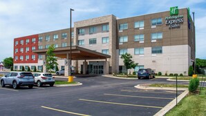 Un bâtiment de la chaîne Holiday Inn Express & Suites, doté d’un design moderne, avec une entrée abritée et un parking pouvant accueillir plusieurs voitures.