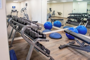 Uma academia com equipamentos de ginástica, bolas azuis de exercício e um espelho refletindo os equipamentos.