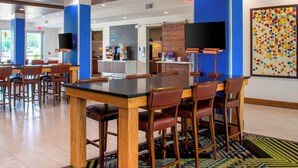A modern restaurant with a large glass table and wooden chairs, a coffee station, and a colorful geometric wall art piece. - Holiday Inn Express & Suites Yorkville by IHG (Yorkville)