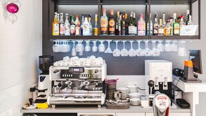 A bar area with a coffee machine, shelves of liquor bottles, and hanging wine glasses. - Merci Boutique Hotel (Kraków)