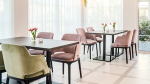 A dining area with tables and chairs, large windows with sheer curtains, and wall-mounted light fixtures. - Merci Boutique Hotel (Kraków)