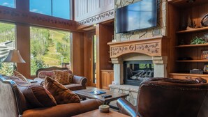 A cozy living room with leather sofas, a stone fireplace, and a large TV mounted on the wall. - 3bd + Loft With Ski In/out Access And Panoramic Views! 3 Bedroom Condo by RedAwning (Avon)
