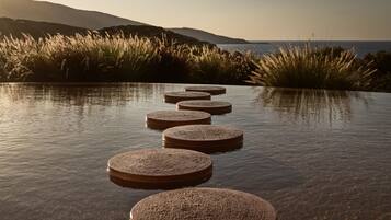 A series of circular stone steps leading into a body of water, surrounded by grass and hills in the background.