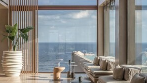 A modern interior with a large window overlooking the ocean, a wooden ceiling, and a seating area with cushions. - Acro Wellness Suites - Adults Only (Malevizi)
