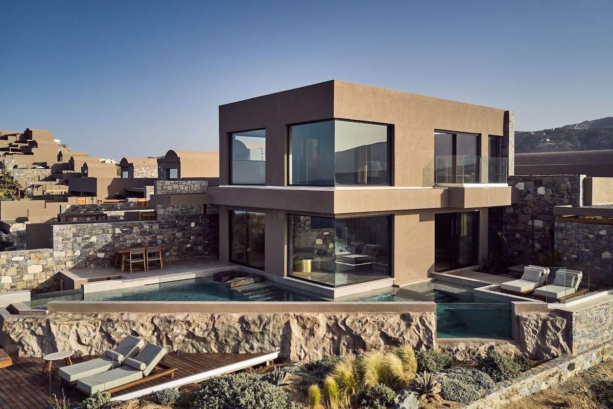A modern villa with a pool, stone walls, and a view of the surrounding landscape.