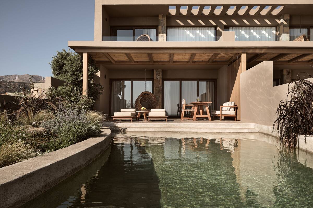 A modern building with a pool, outdoor seating, and a view of the landscape.