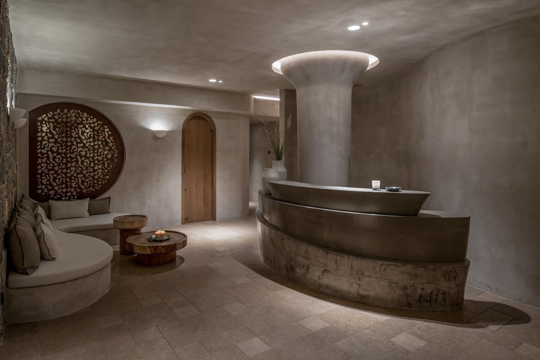 Un espace de spa moderne avec un comptoir d’accueil incurvé, un coin salon circulaire et une porte en bois.