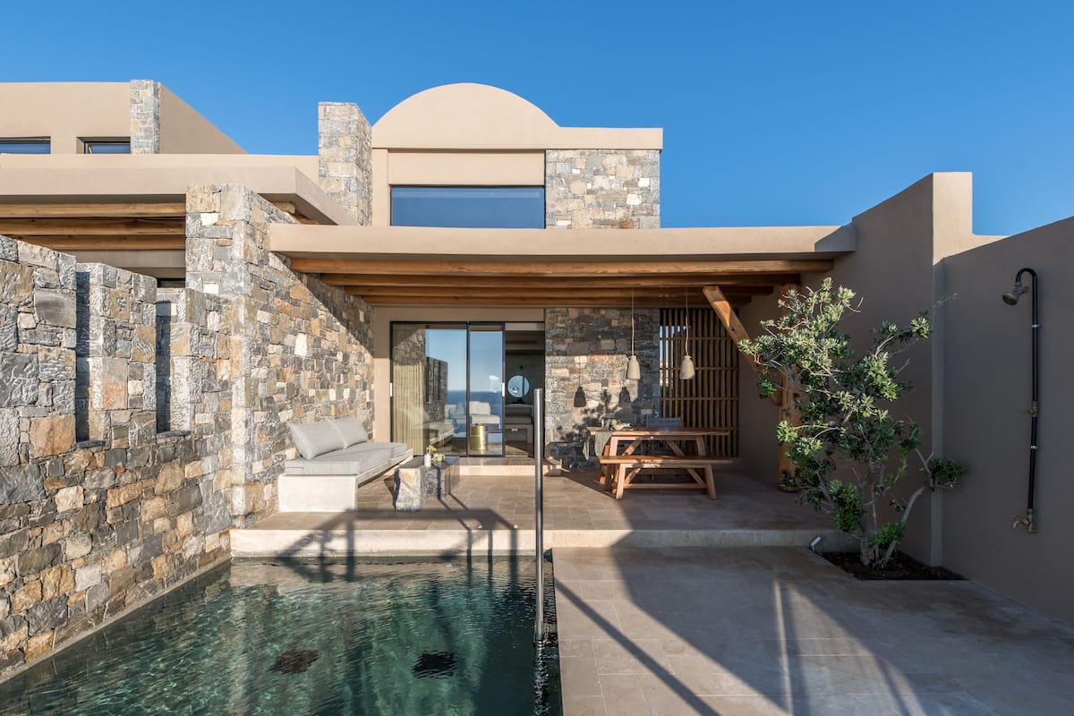 A modern house with a stone exterior, a swimming pool, and a patio area with outdoor furniture.