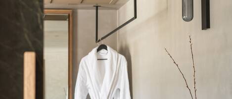 Een moderne badkamer met een houten vloer, een donker houten wastafelmeubel, een witte badjas die aan een rek hangt, en een vaas met takken op het wastafelmeubel.